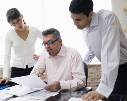 Three people standing around a table in an office.