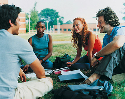 Smiling college students sitting in a circle on the grass.